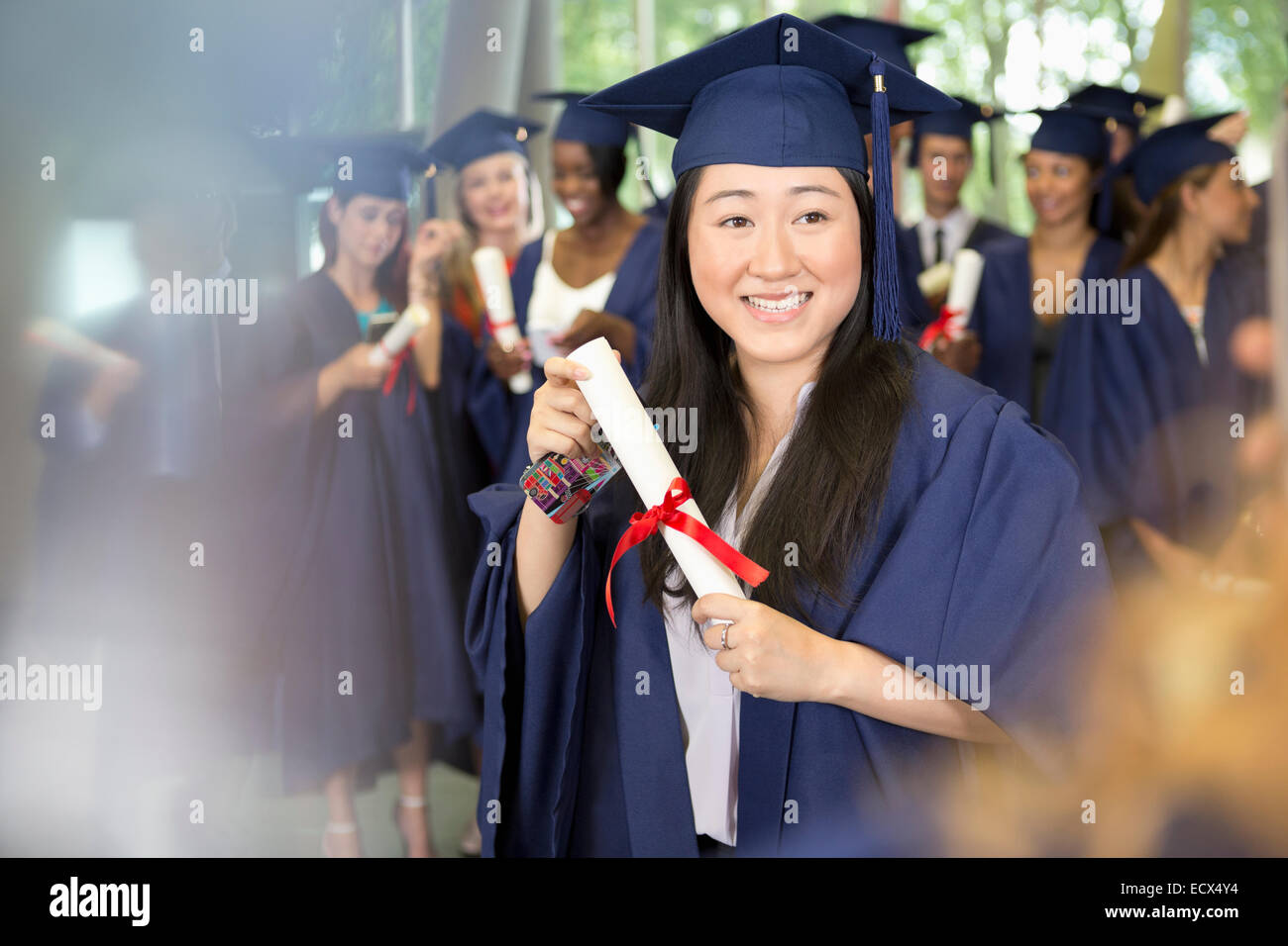 Portrait of smiling female student in graduation gown holding diploma Stock Photo