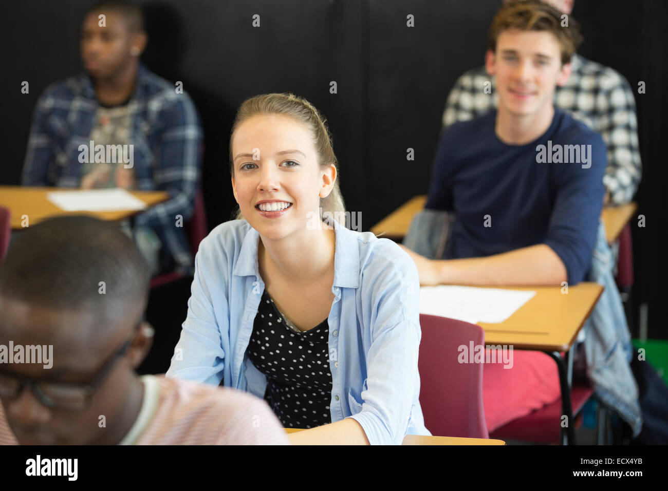 View of smiling students sitting at desks in classroom Stock Photo