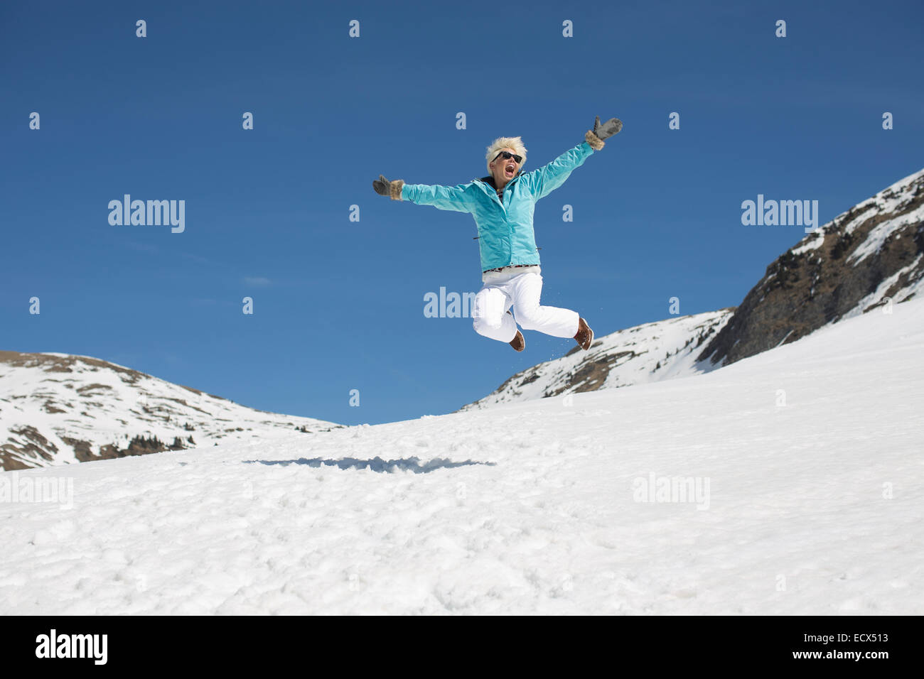 Exuberant woman jumping in snow Stock Photo