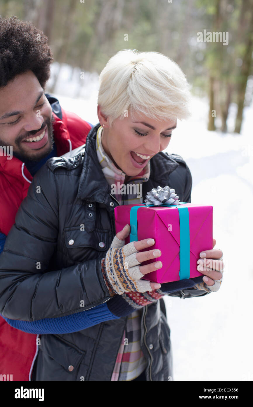 Man surprising woman with Christmas gift in snow Stock Photo