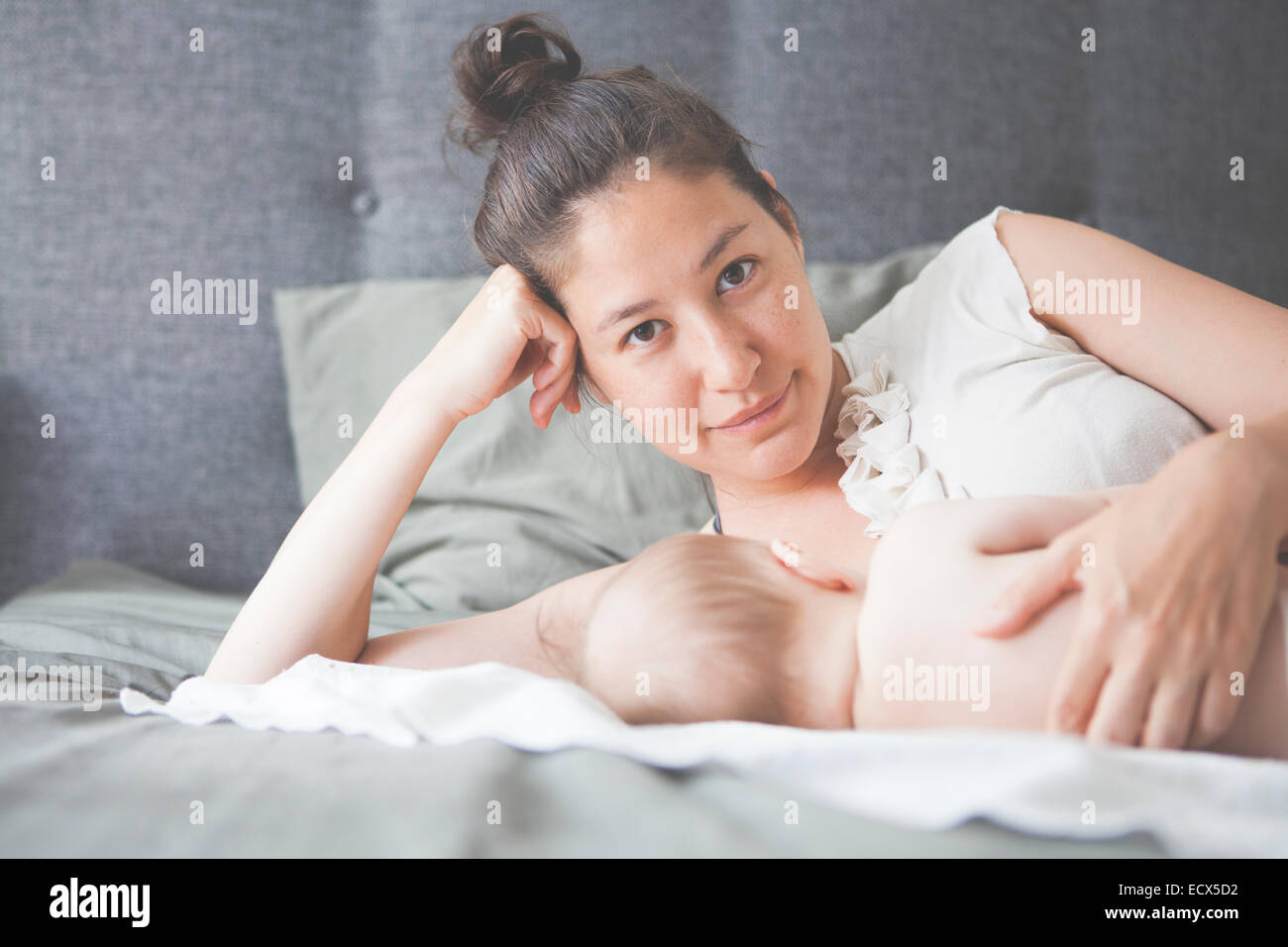 Portrait of mother holding baby lying on bed and smiling Stock Photo