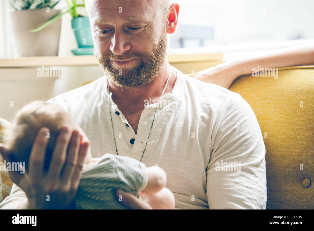 Portrait of father holding baby, sitting on sofa beside mother Stock Photo