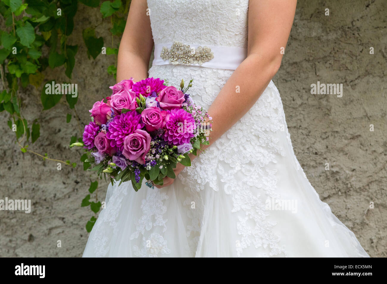 A beautiful bride holding her purple bouquet of flowers Stock Photo