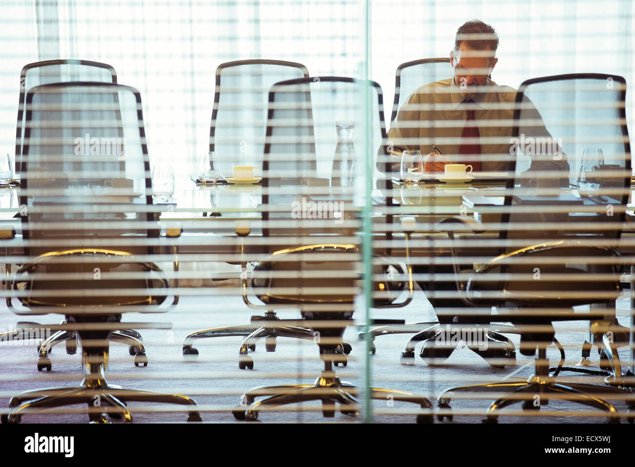 Businessman sitting behind blinds in conference room Stock Photo