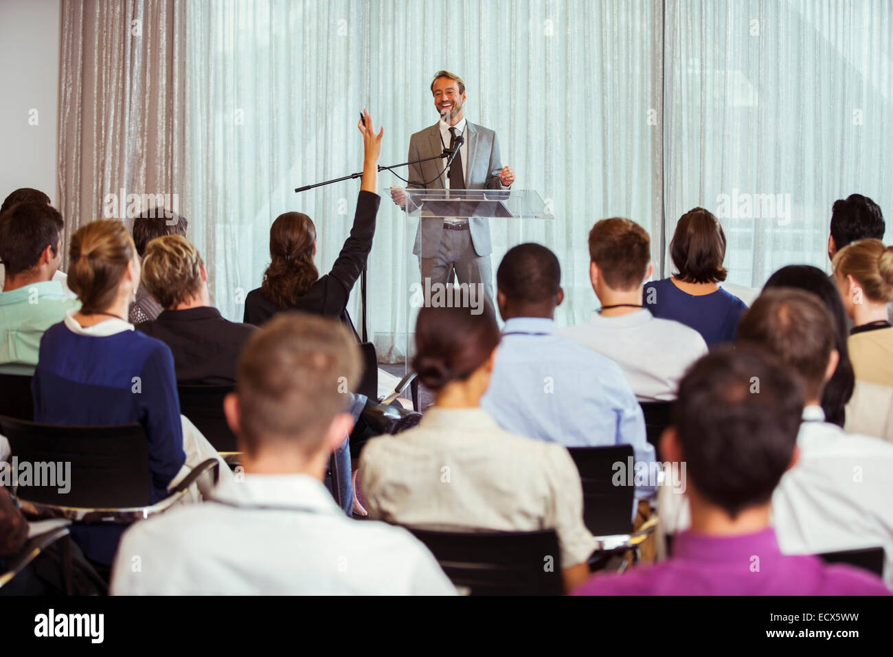 Businessman giving speech in conference room, woman from audience raising hand Stock Photo