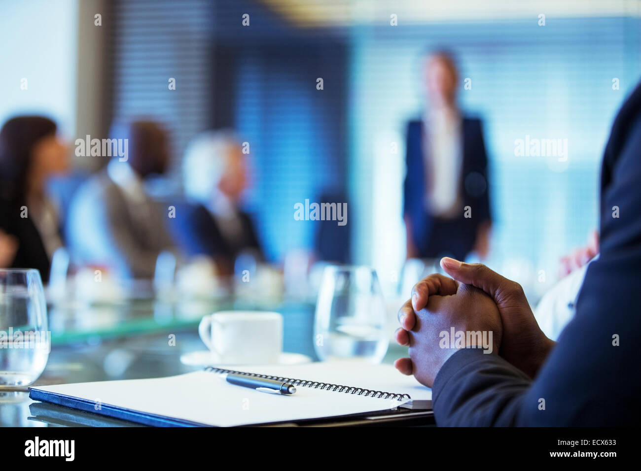 Businessman sitting at conference table in conference room with hands clasped Stock Photo