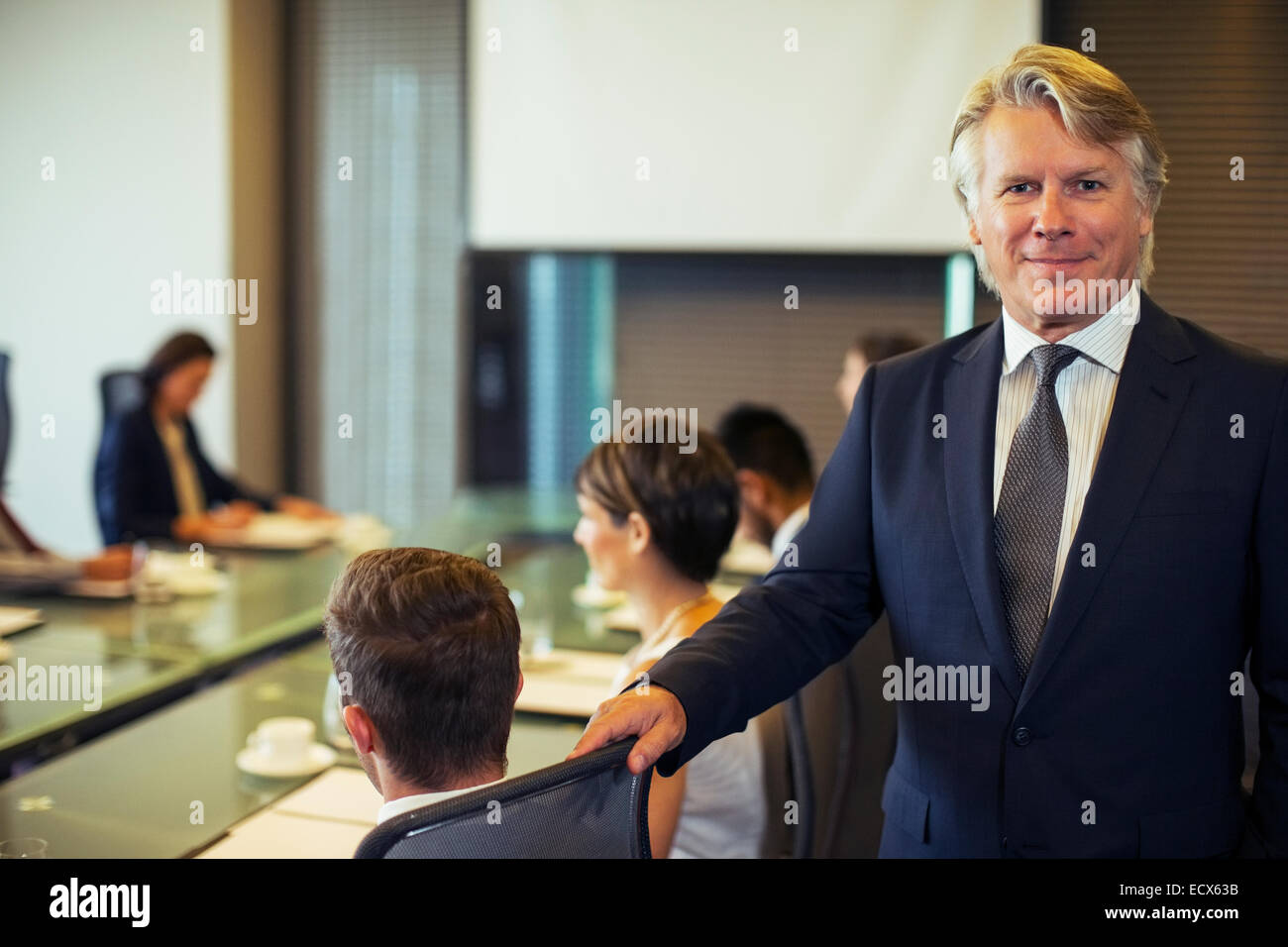 Portrait of businessman standing in conference room with colleagues in background Stock Photo