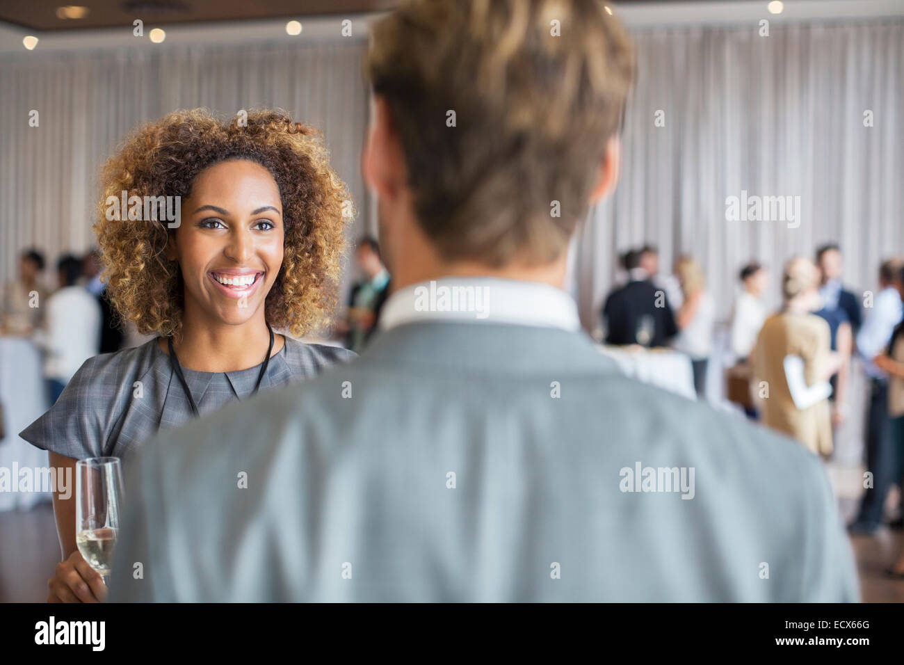 Two business people standing with champagne flutes, smiling and talking in conference room Stock Photo