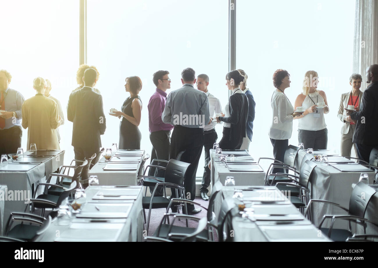 Group of people standing by windows of conference room, socializing during coffee break Stock Photo