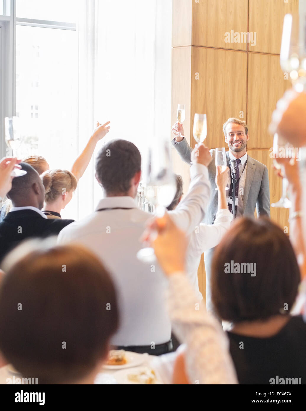 Portrait of smiling man standing before audience in conference room, raising toast with champagne flute Stock Photo