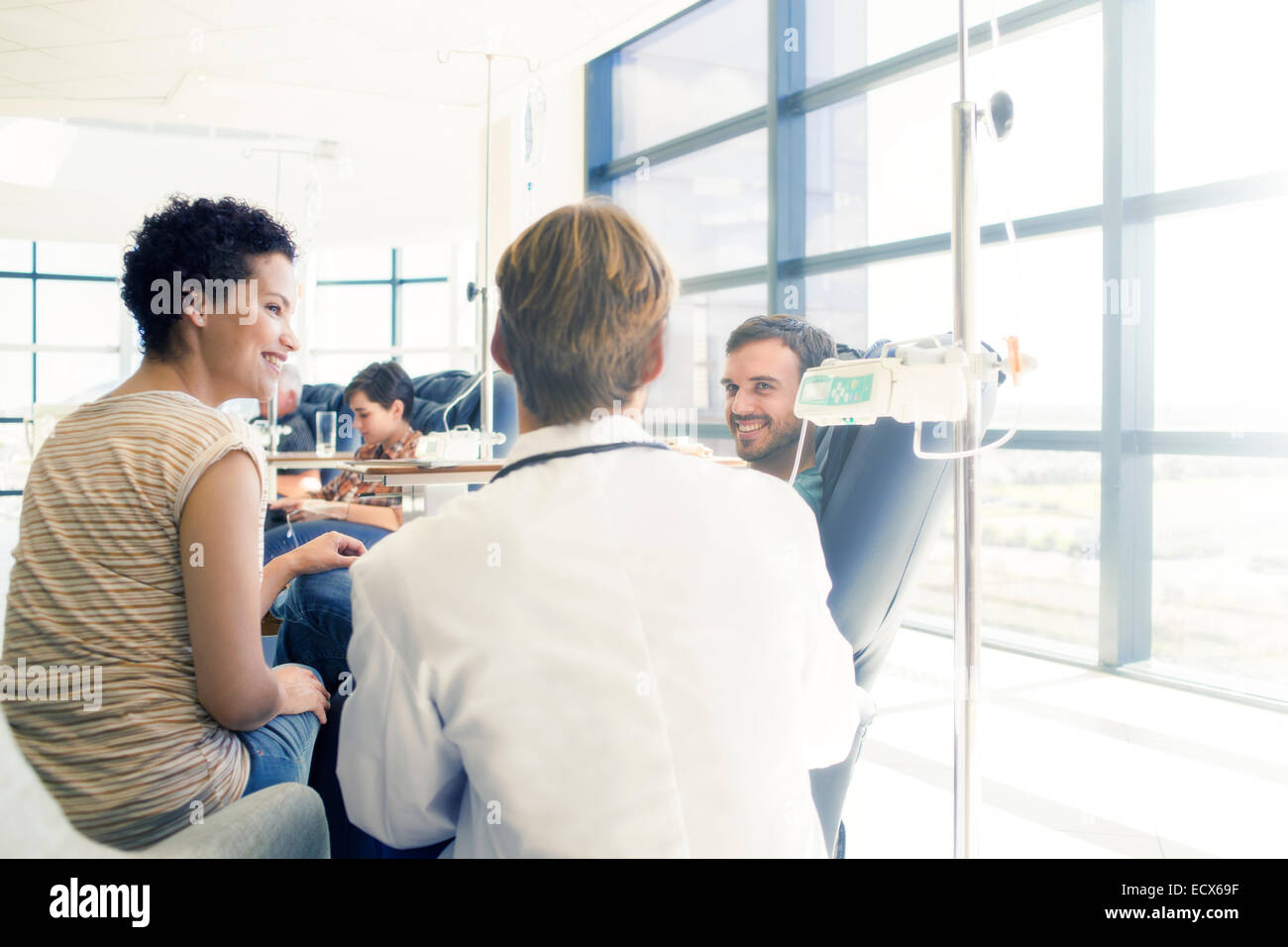 Doctor talking to patient receiving medical treatment in hospital ward Stock Photo