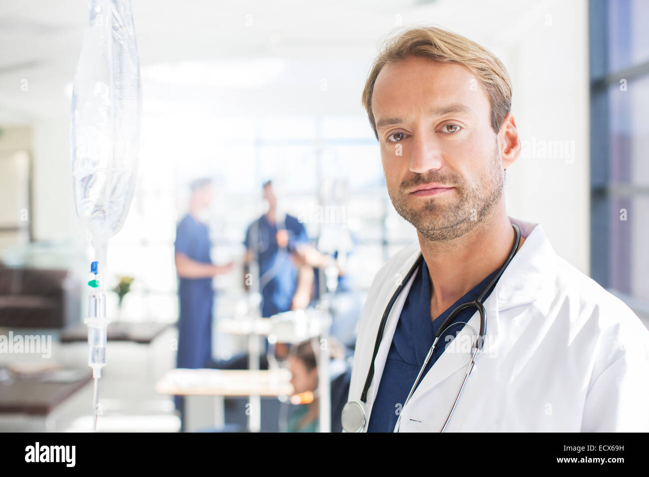Portrait of mid adult doctor with colleagues in background, standing in hospital ward Stock Photo