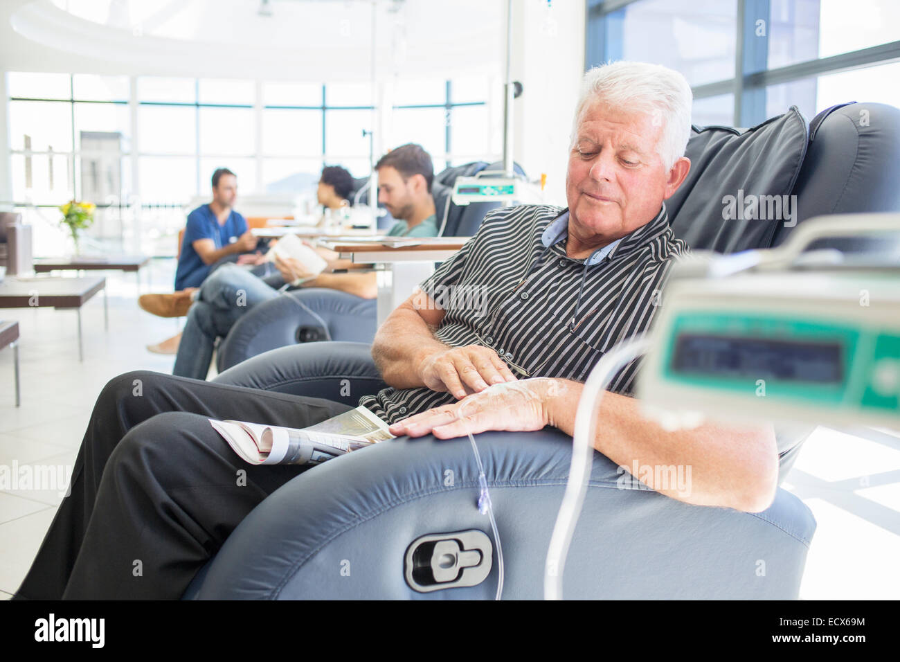 Senior patient receiving medical treatment sitting and looking down in hospital ward Stock Photo