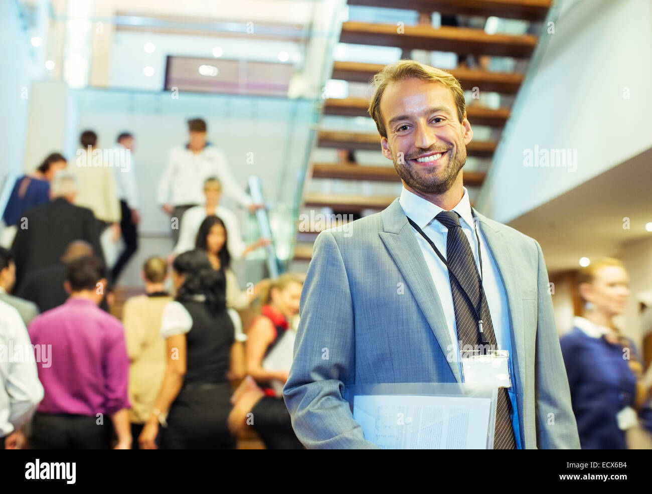 Portrait of smiling businessman holding file, standing in crowded lobby of conference center Stock Photo