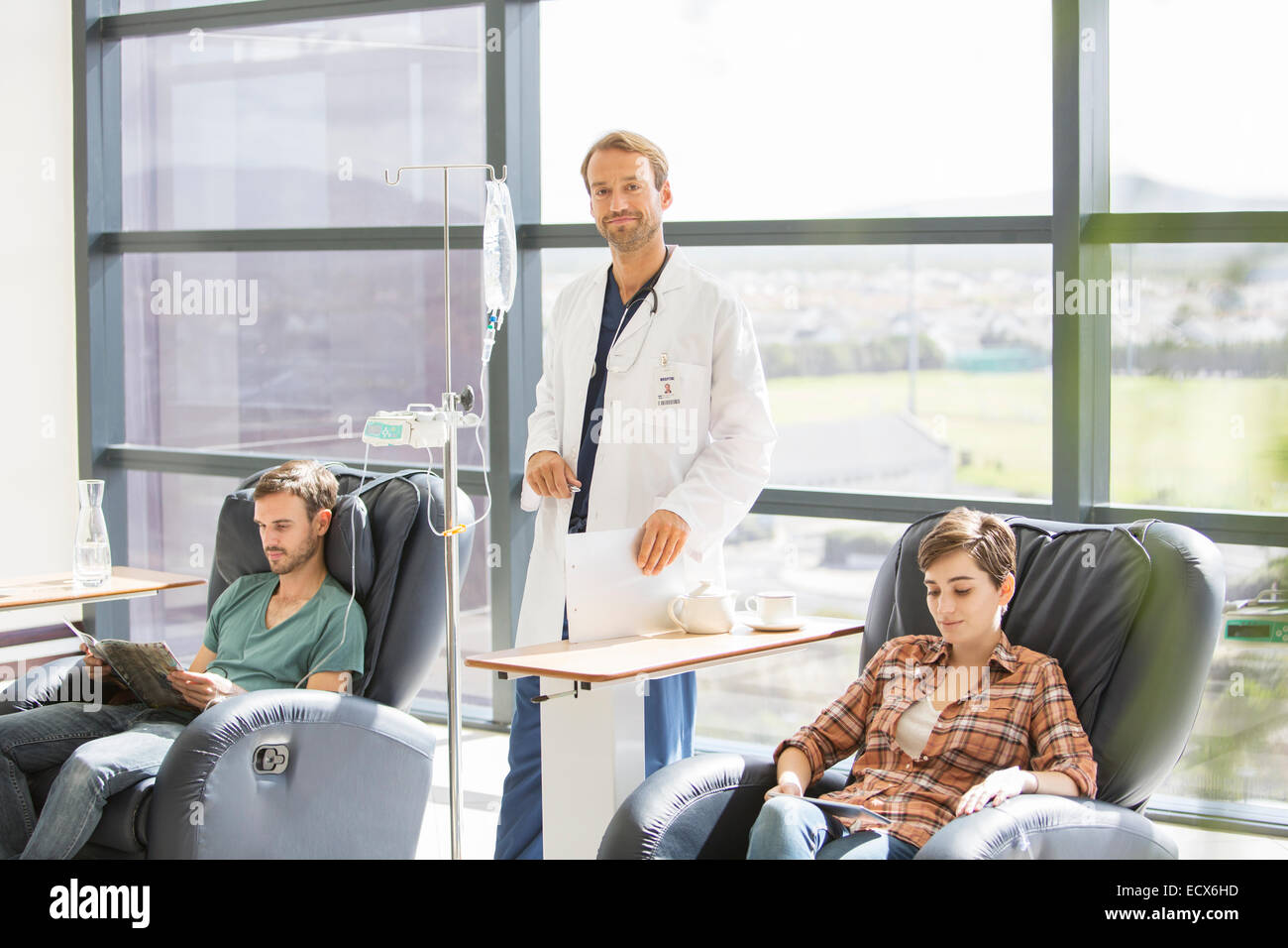 Doctor attending patients receiving intravenous infusion in hospital Stock Photo