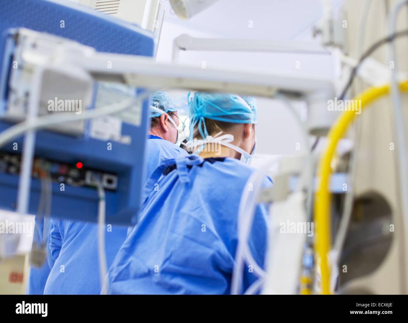 Rear view of doctors in operating theater, medical equipment in foreground Stock Photo