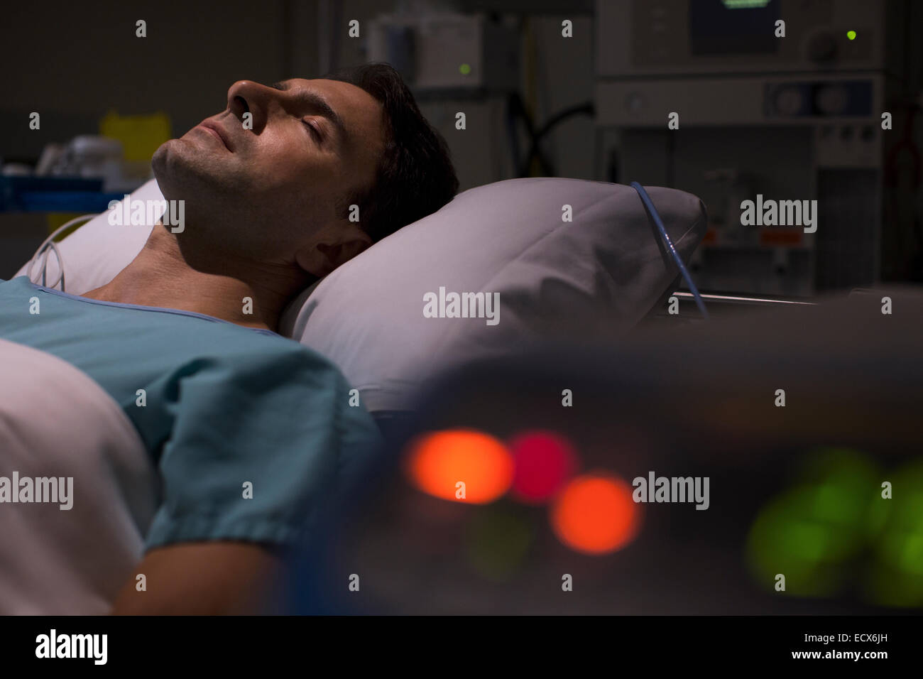 Patient lying in hospital bed in intensive care unit, medical equipment in foreground Stock Photo