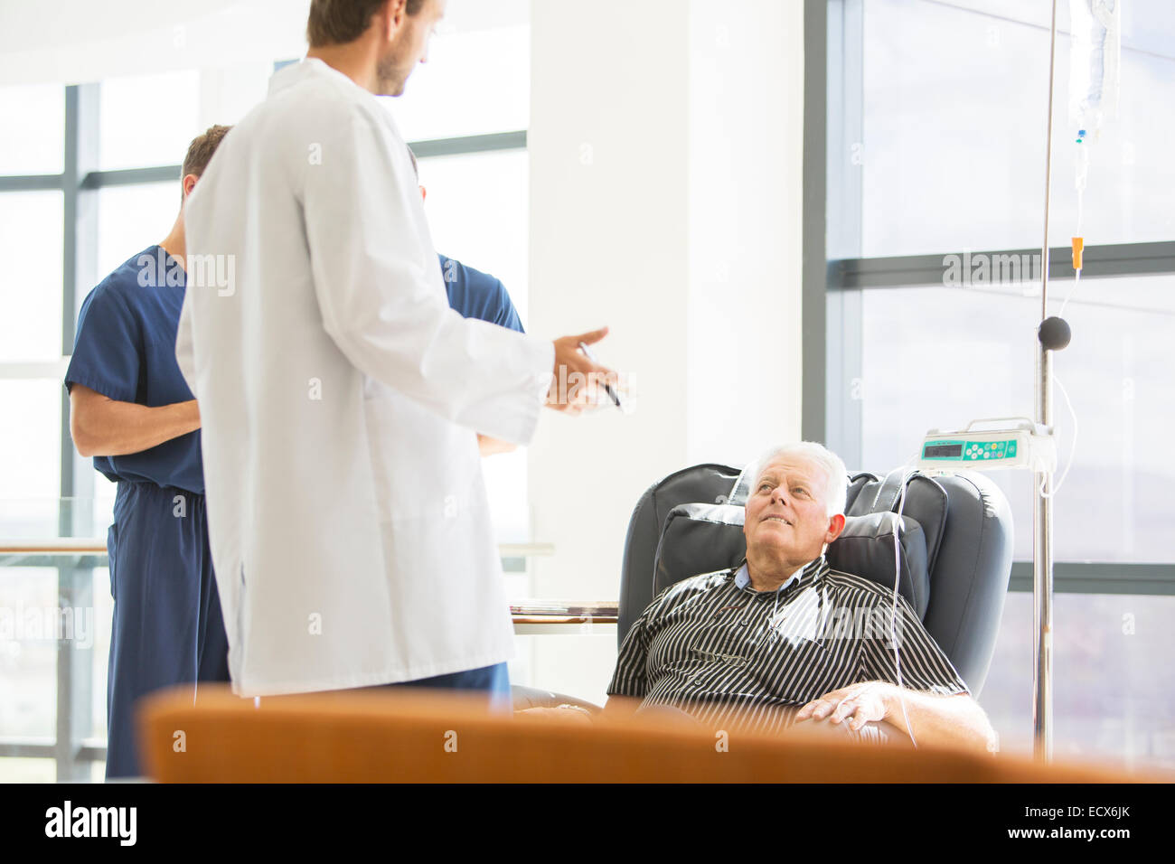 Two doctors talking to senior patient undergoing medical treatment in outpatient clinic Stock Photo