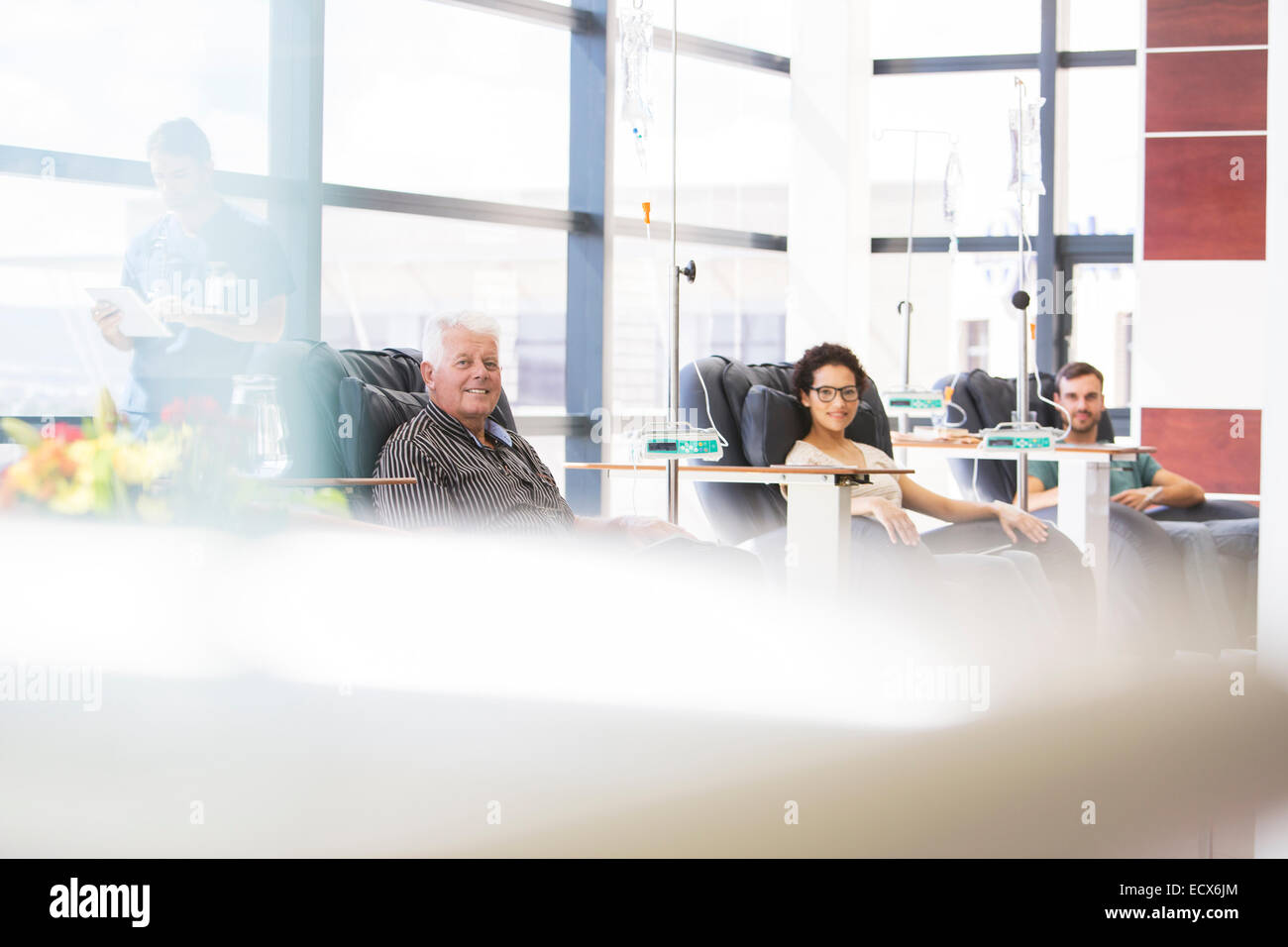 Three patients sitting in armchairs, undergoing medical treatment in outpatient clinic Stock Photo