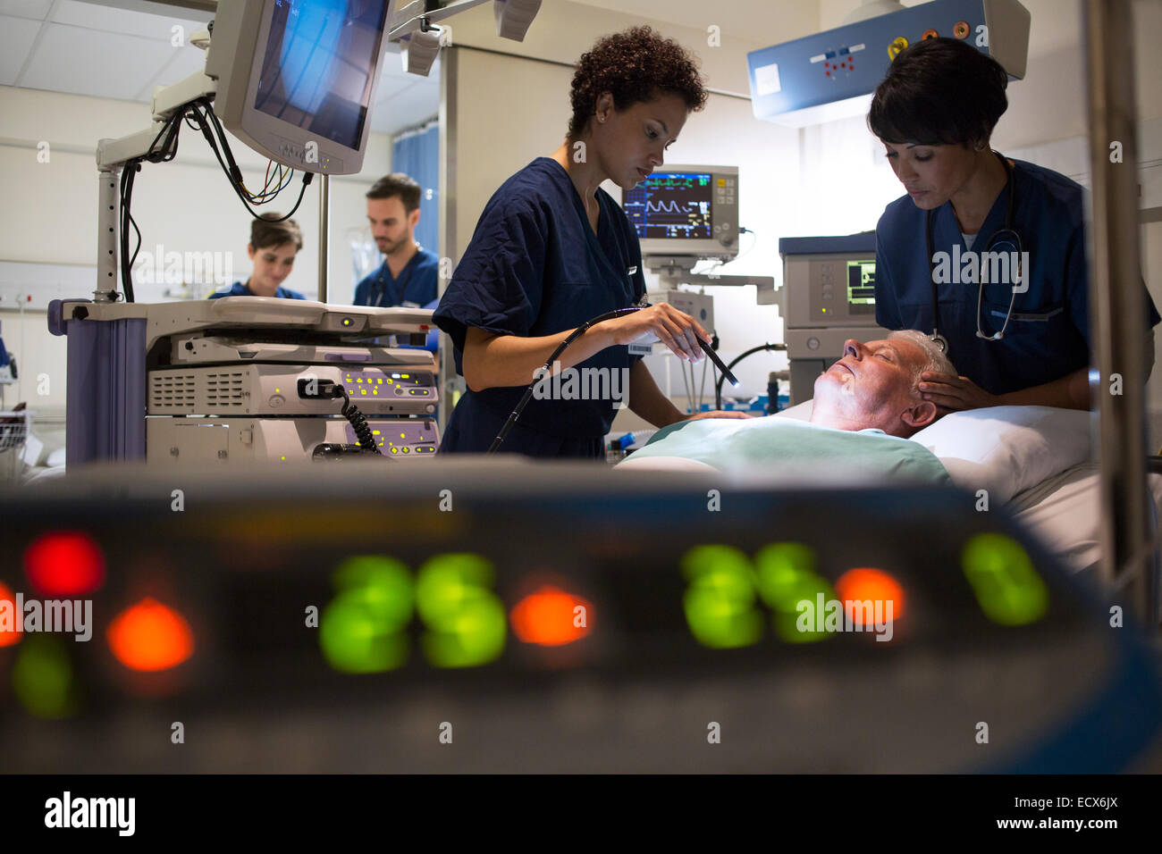 Doctors attending patient in intensive care unit, monitoring equipment in foreground Stock Photo