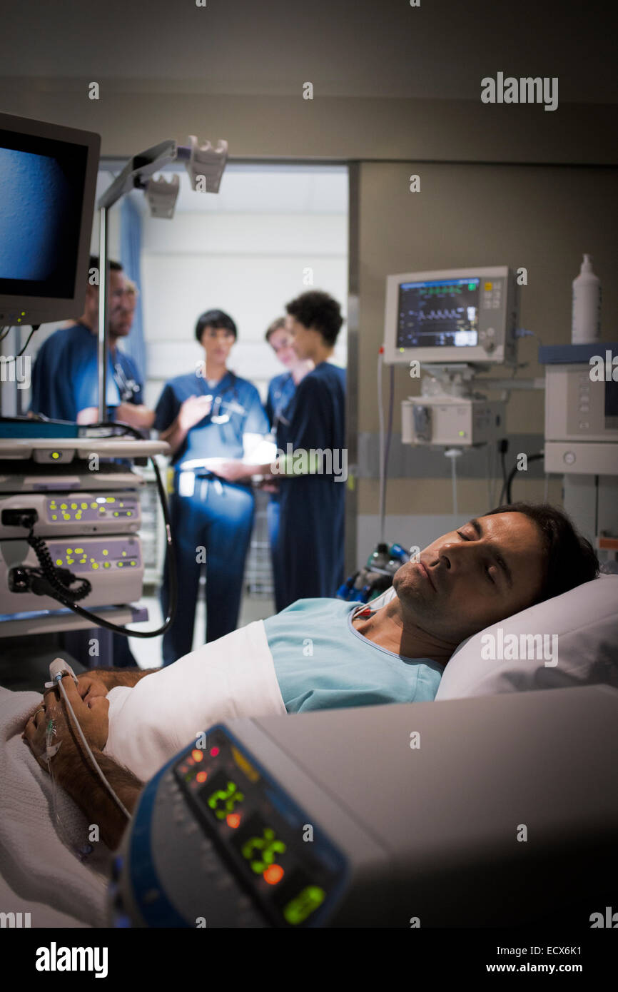 Patient lying in bed in intensive care unit, doctors discussing in background Stock Photo