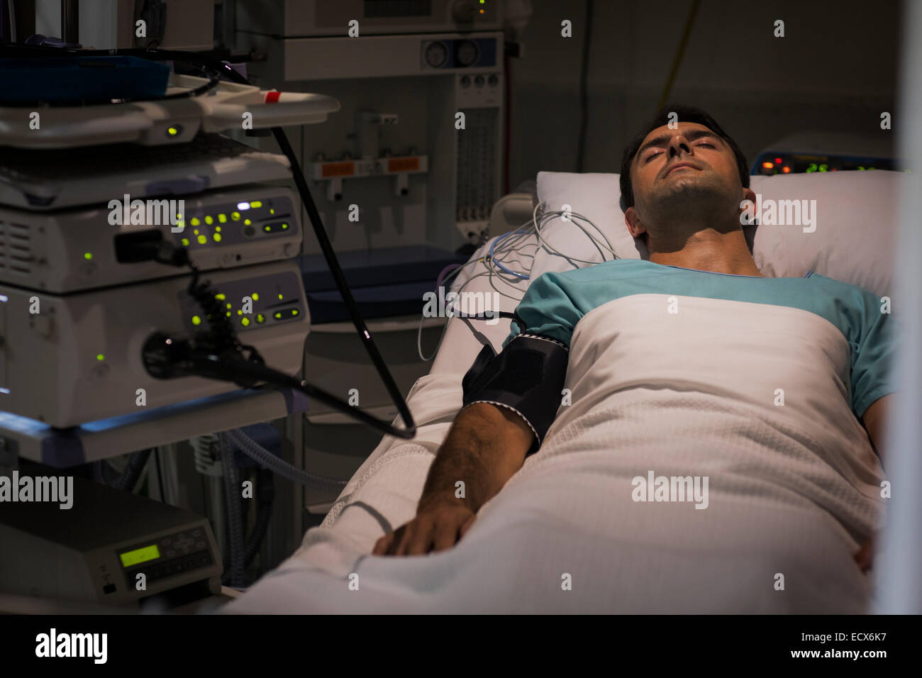 Patient lying in bed, attached to monitoring equipment in intensive care unit Stock Photo
