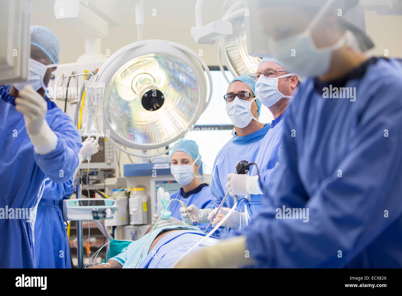 Doctors performing surgery in operating theater, looking at monitor Stock Photo