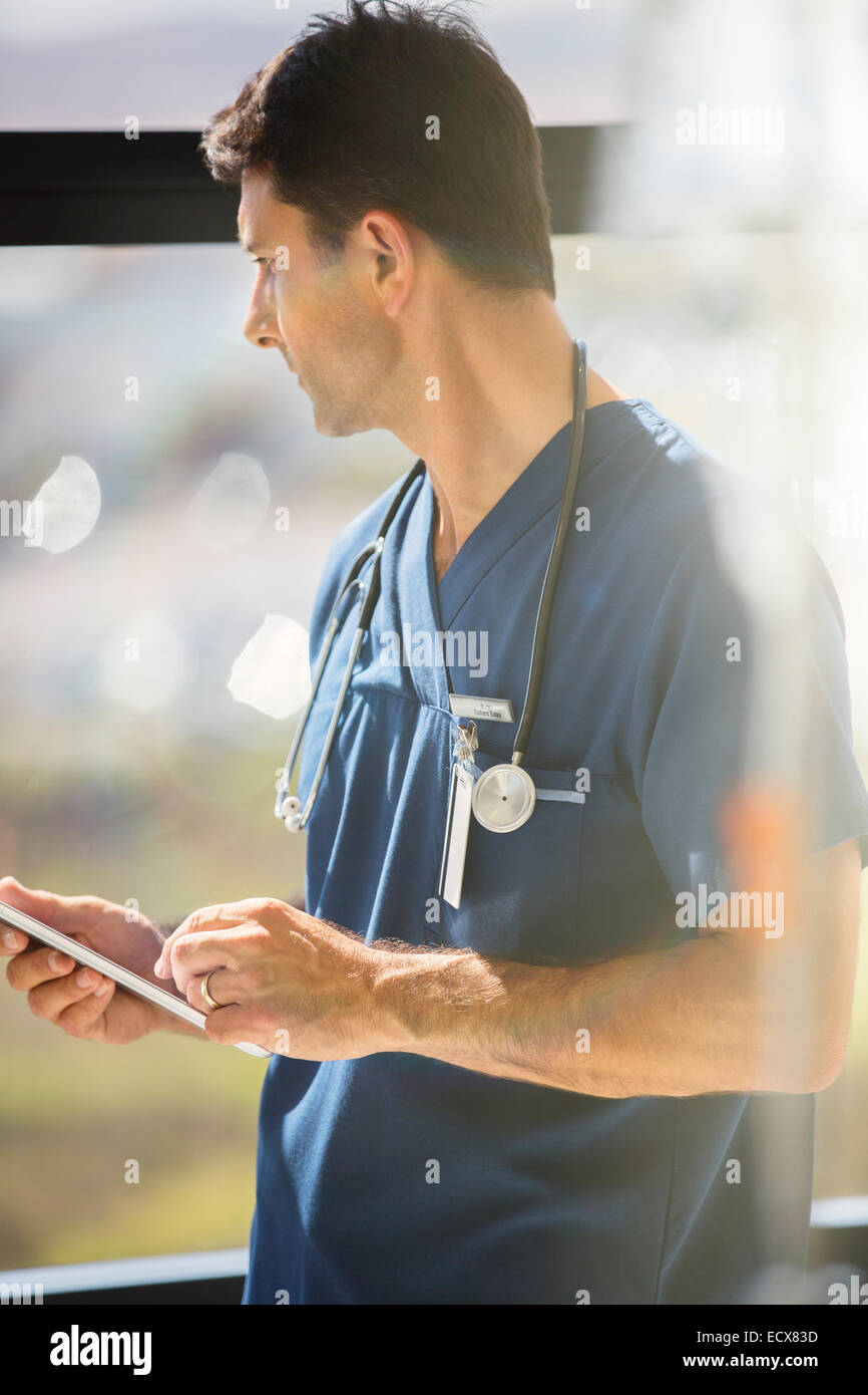 Male doctor holding tablet pc and looking out of hospital window Stock Photo