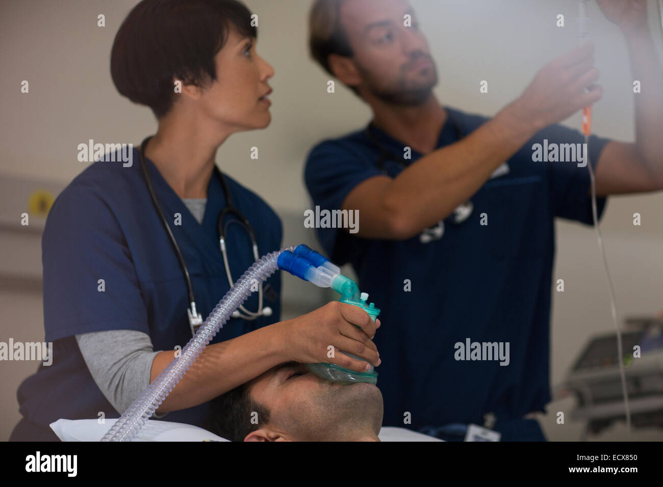 Doctor holding oxygen mask over patient, doctor adjusting IV drip in intensive care unit Stock Photo