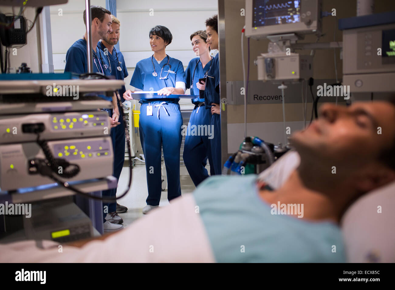 Patient attached to medical monitoring equipment in intensive care unit, doctors standing in doorway Stock Photo