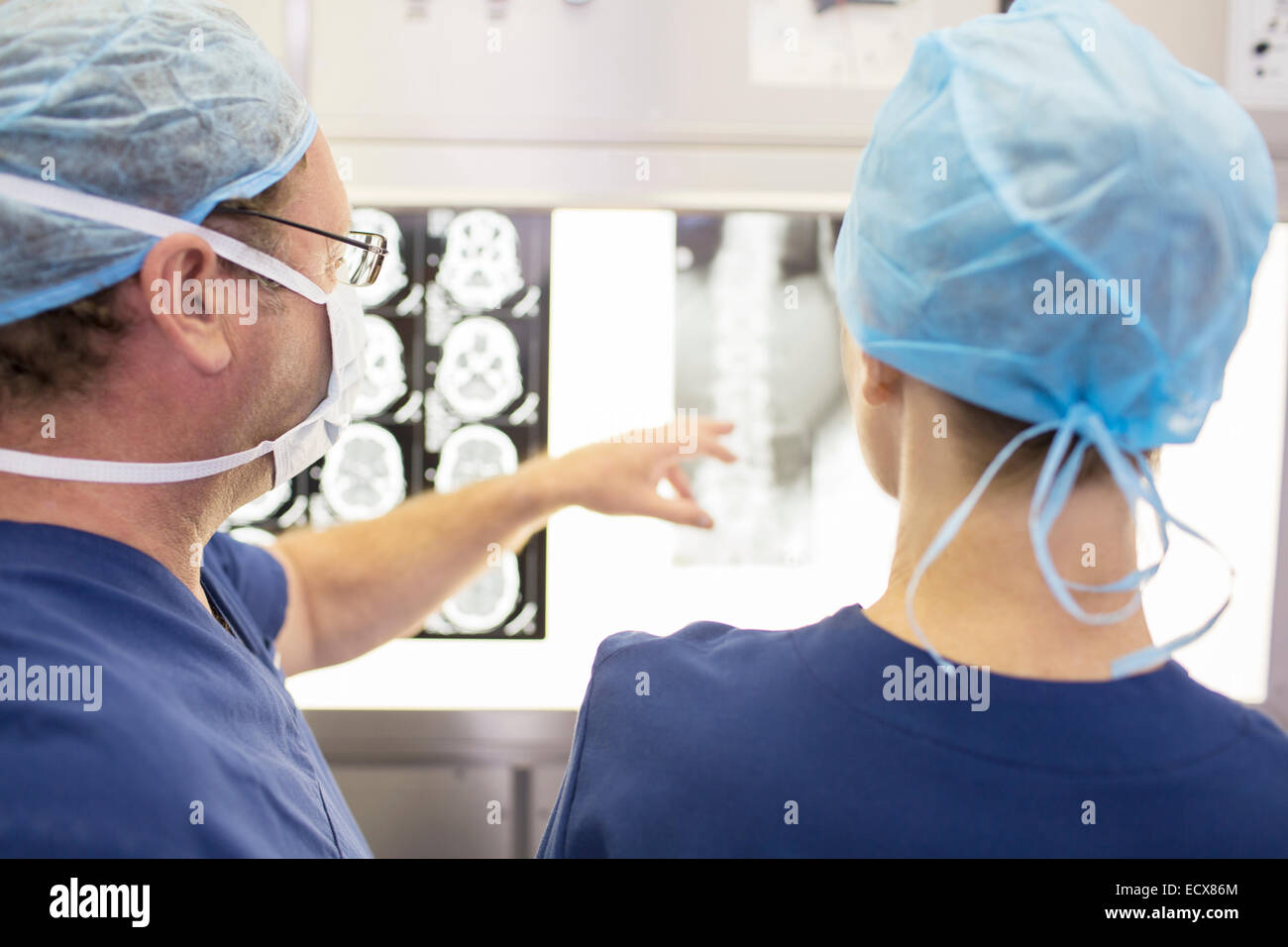 Rear view of surgeons looking at patient's x-ray and MRI scan in operating theater Stock Photo