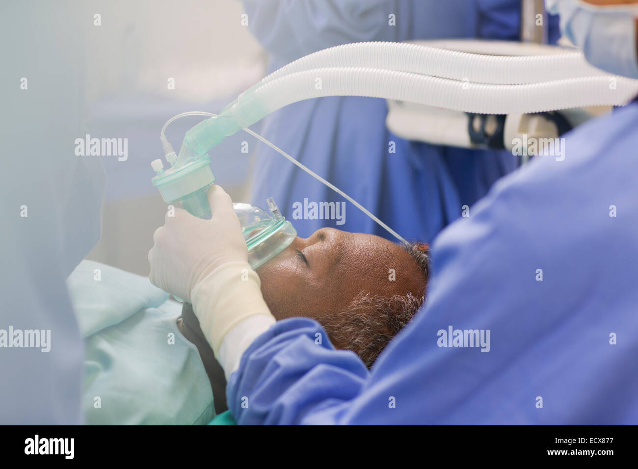 Close up of doctor wearing surgical gloves, holding oxygen mask over patient in operating theater Stock Photo
