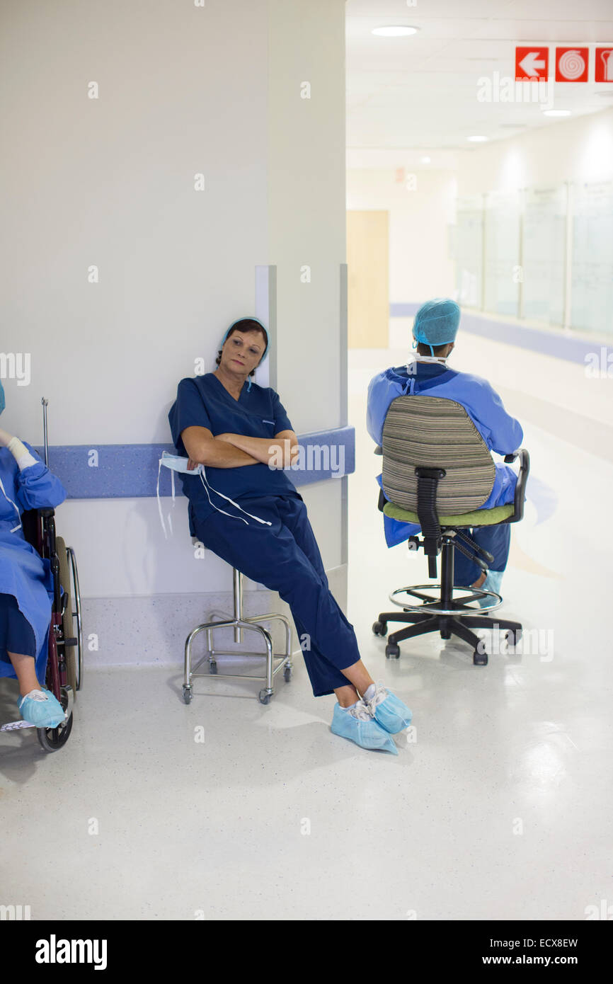 Two doctors wearing surgical clothing resting in hospital corridor
