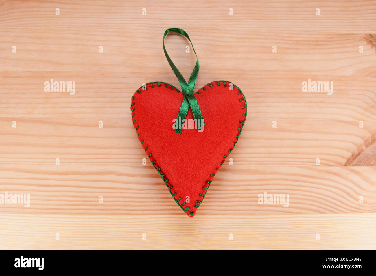Red felt heart-shaped hanging decoration with green ribbon on a wooden table Stock Photo