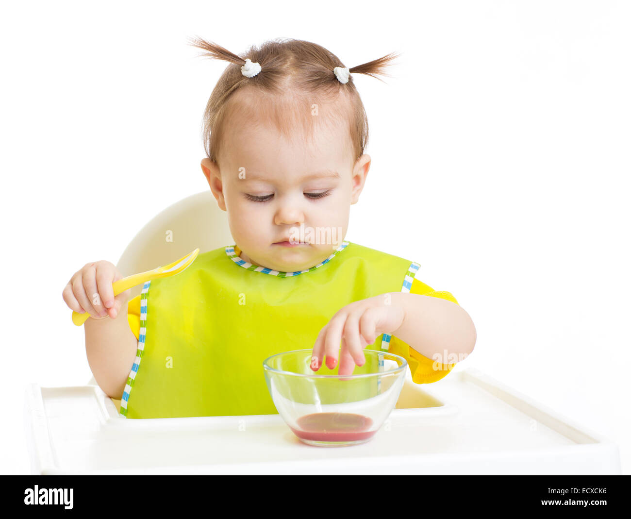 Baby eating and put fingers into food sitting at table Stock Photo