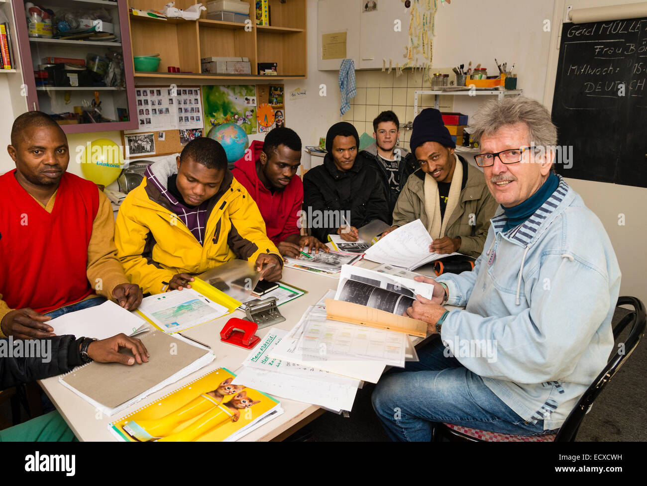 A retired social worker, working as a volunteer now (right), gives a lesson in German language to mostly African refugees. Stock Photo