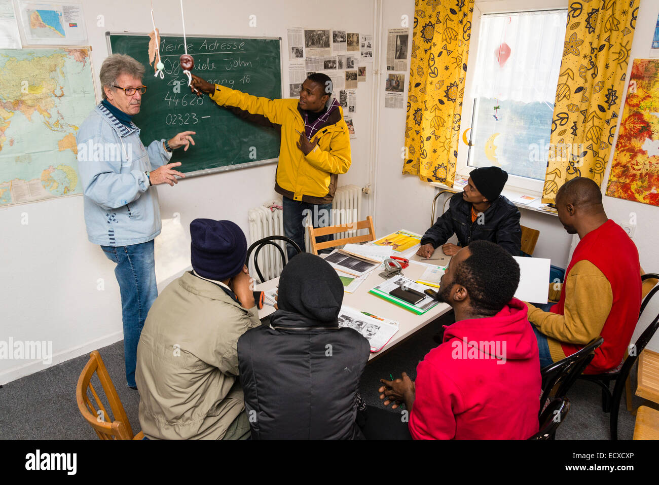 A retired social worker, working as a volunteer now (left), gives a lesson in German language to mostly African refugees. Stock Photo