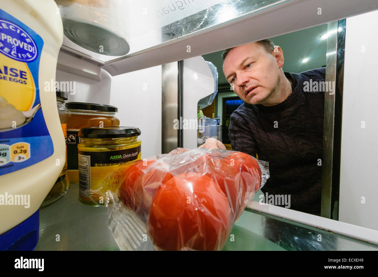 Man takes a packet of tomatoes from a refrigerator Stock Photo