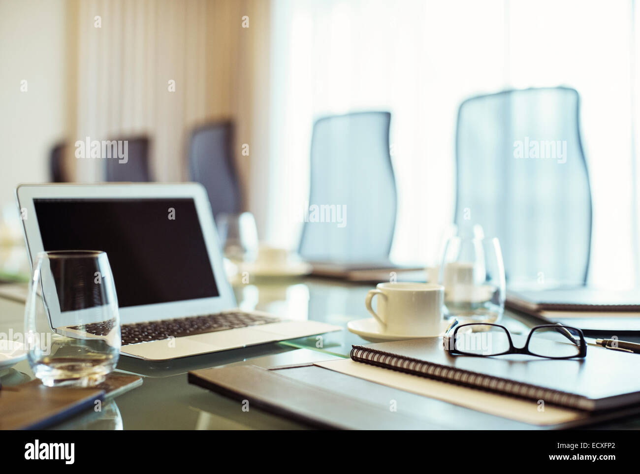 Laptop, eyeglasses and diary on conference table in empty conference room Stock Photo