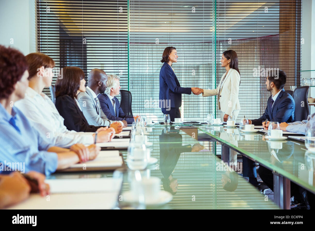 Two businesswomen shaking hands in conference room, colleagues watching Stock Photo