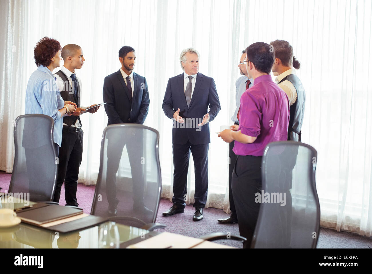 Group of business people standing by window discussing in conference room Stock Photo