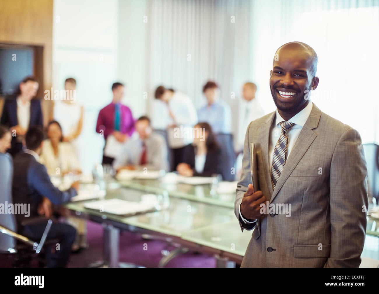 Portrait of smiling young man wearing suit and holding laptop in conference room Stock Photo