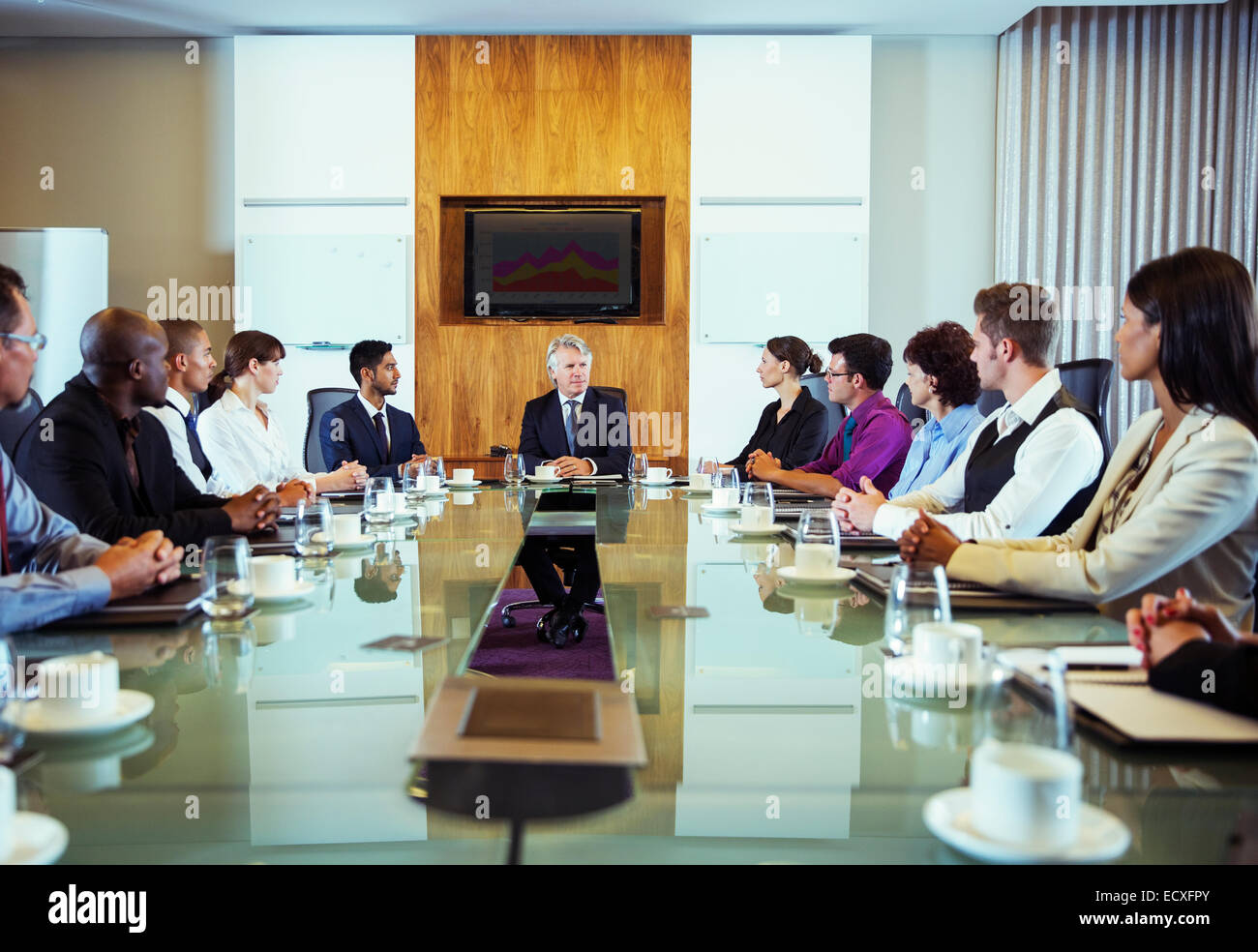 Conference participants looking at man sitting at head of conference table Stock Photo