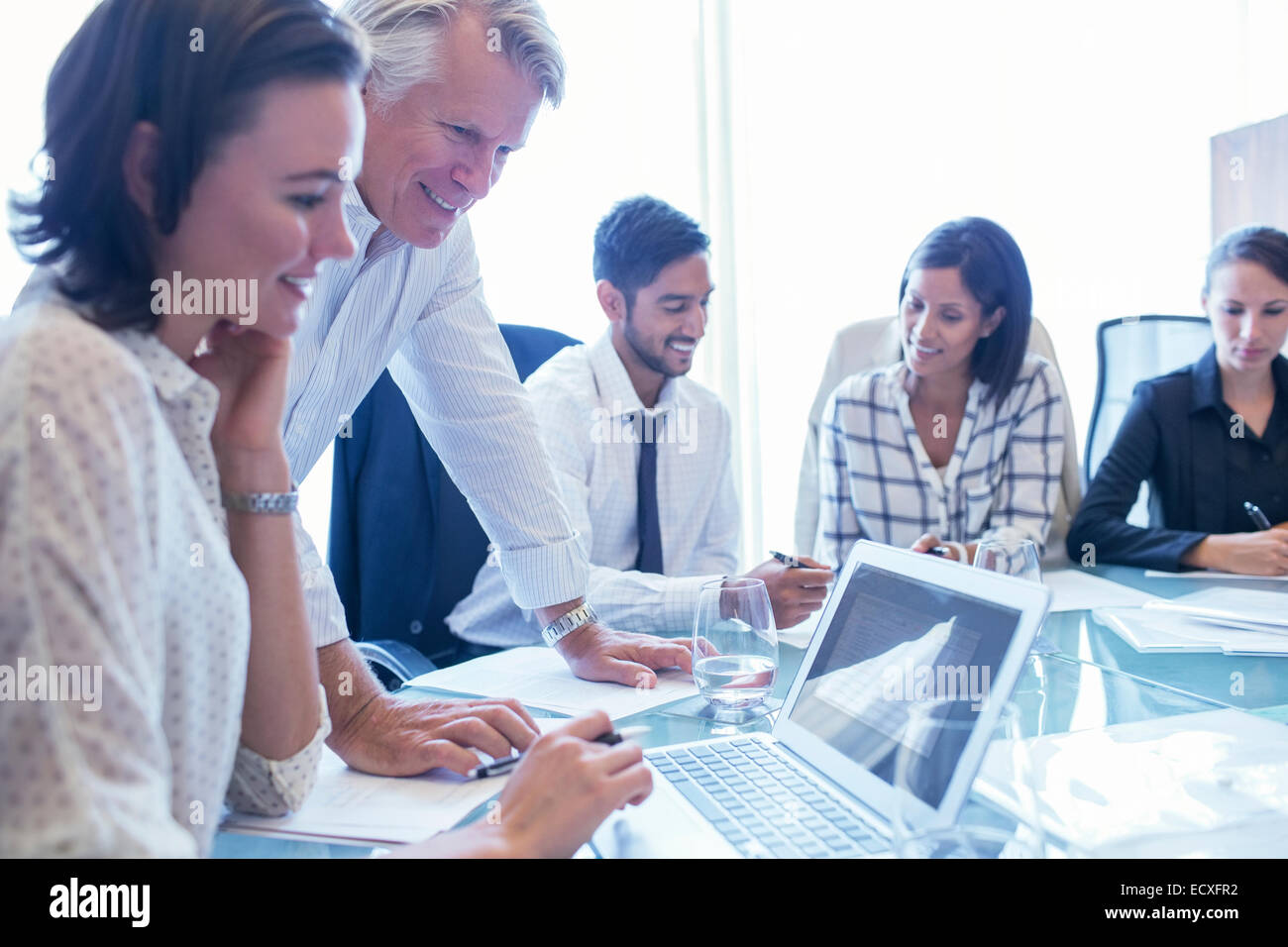Businesswomen and businessmen sitting at conference table, using laptop and smiling Stock Photo