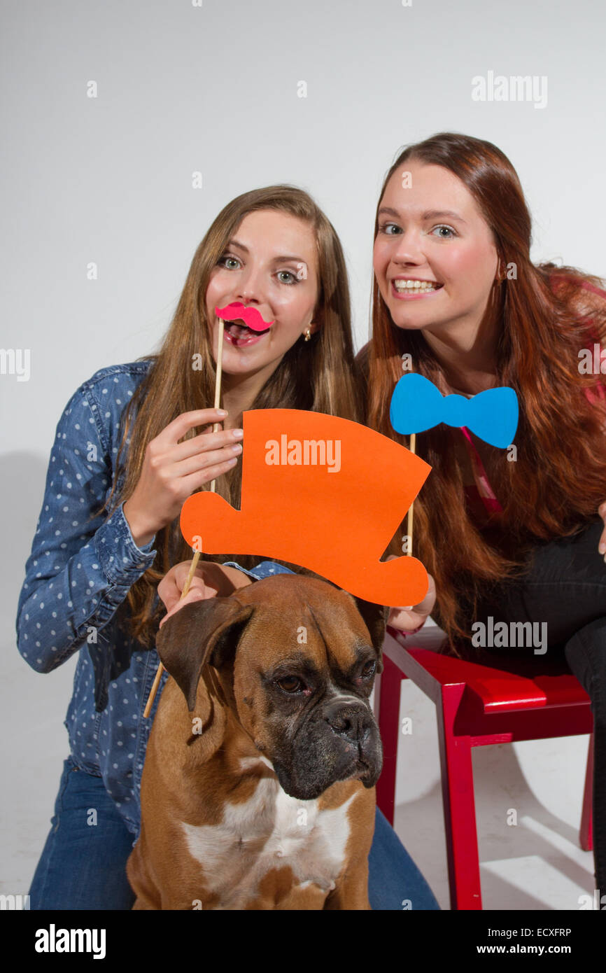 Two young women and a boxer dog enjoying with silly props posing for