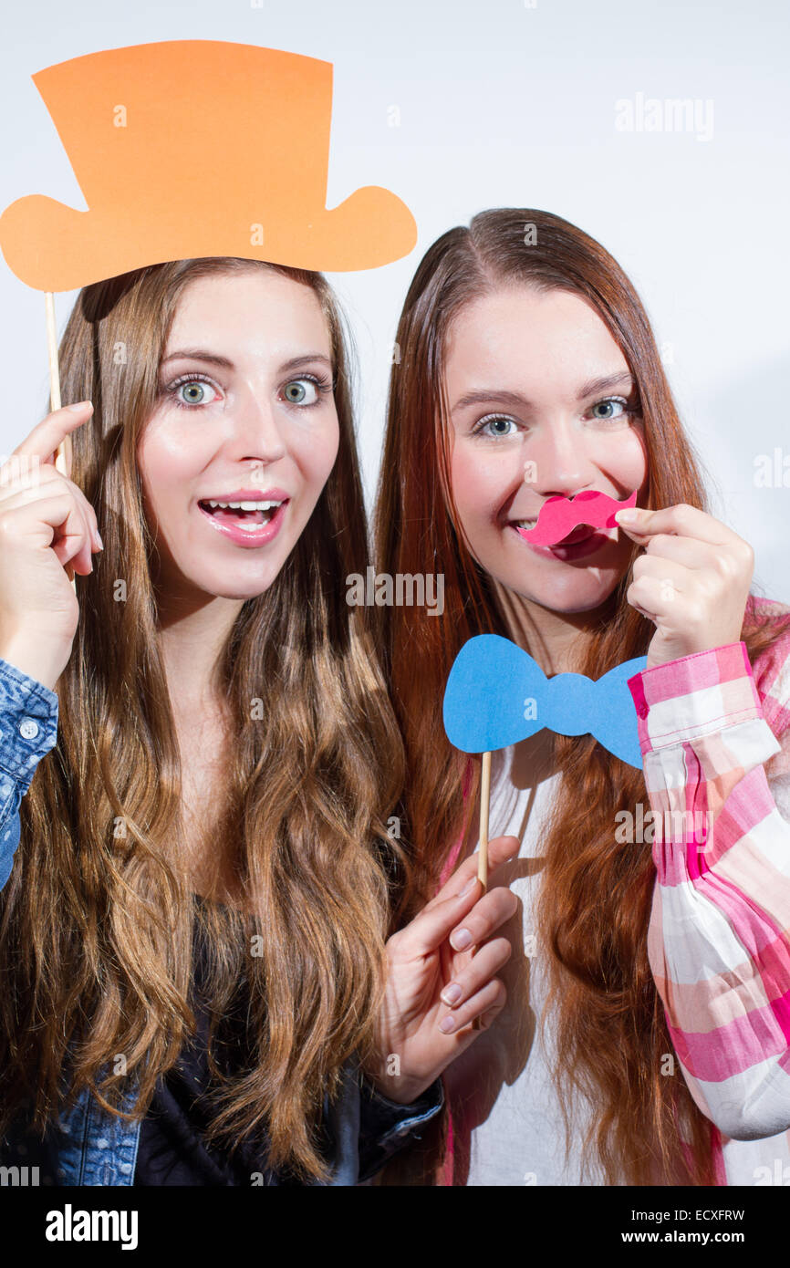 Two young women enjoying with silly props posing for pictures photo booth style Stock Photo