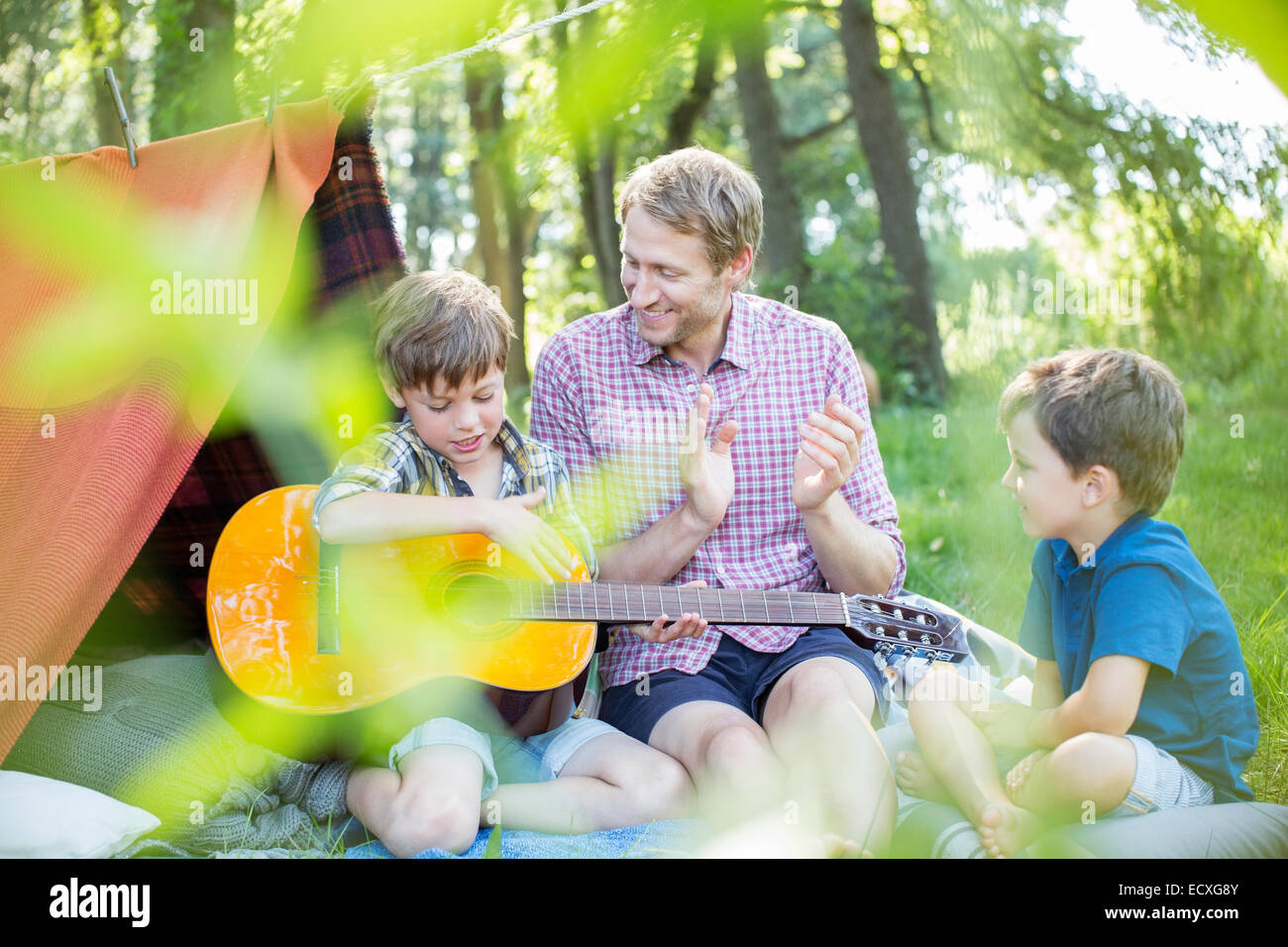 Father and sons playing guitar near camping tent Stock Photo
