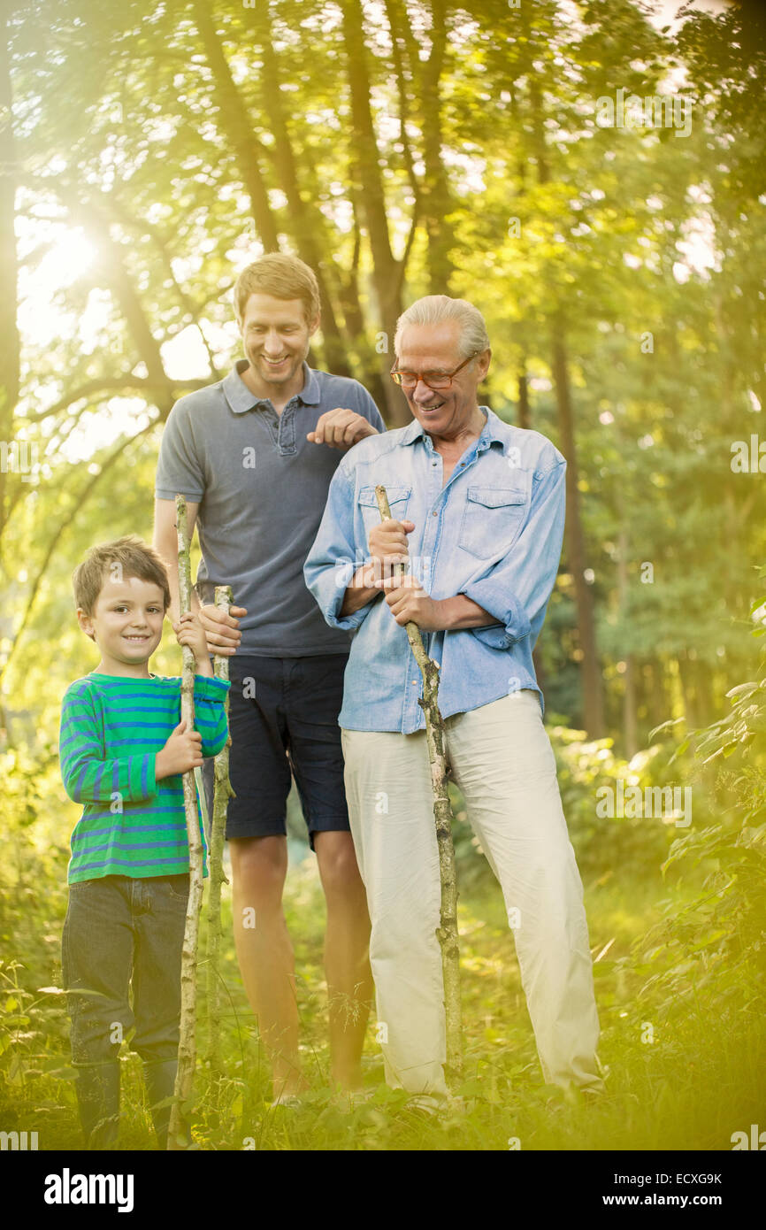 Boy, father and grandfather holding sticks in forest Stock Photo