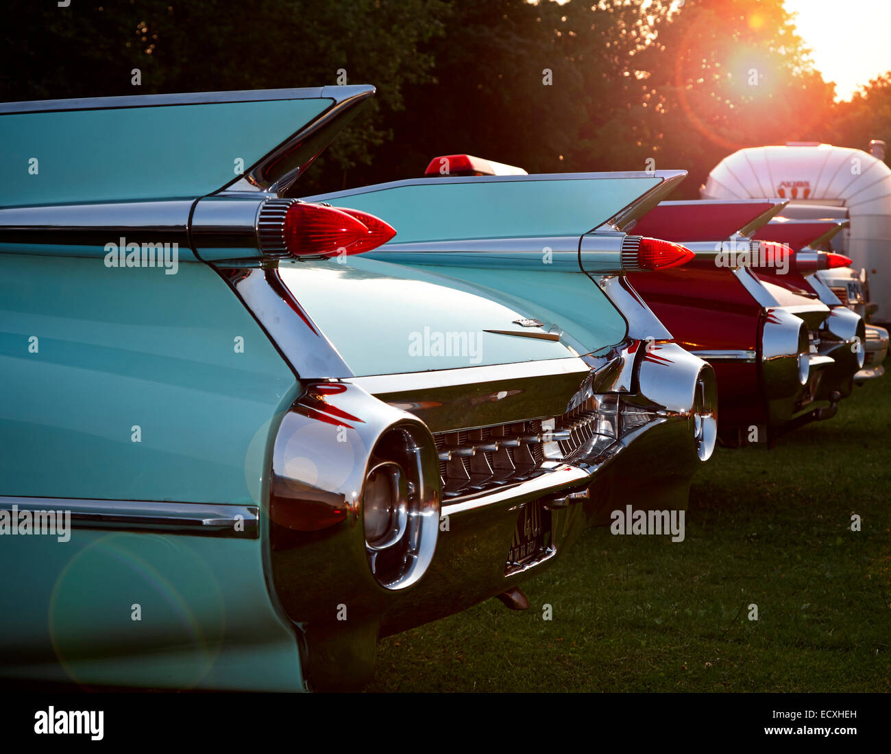 Fins and rear bumpers on two vintage Cadillac Eldorado with American Avion trailer in background with sunburst in sky. Stock Photo