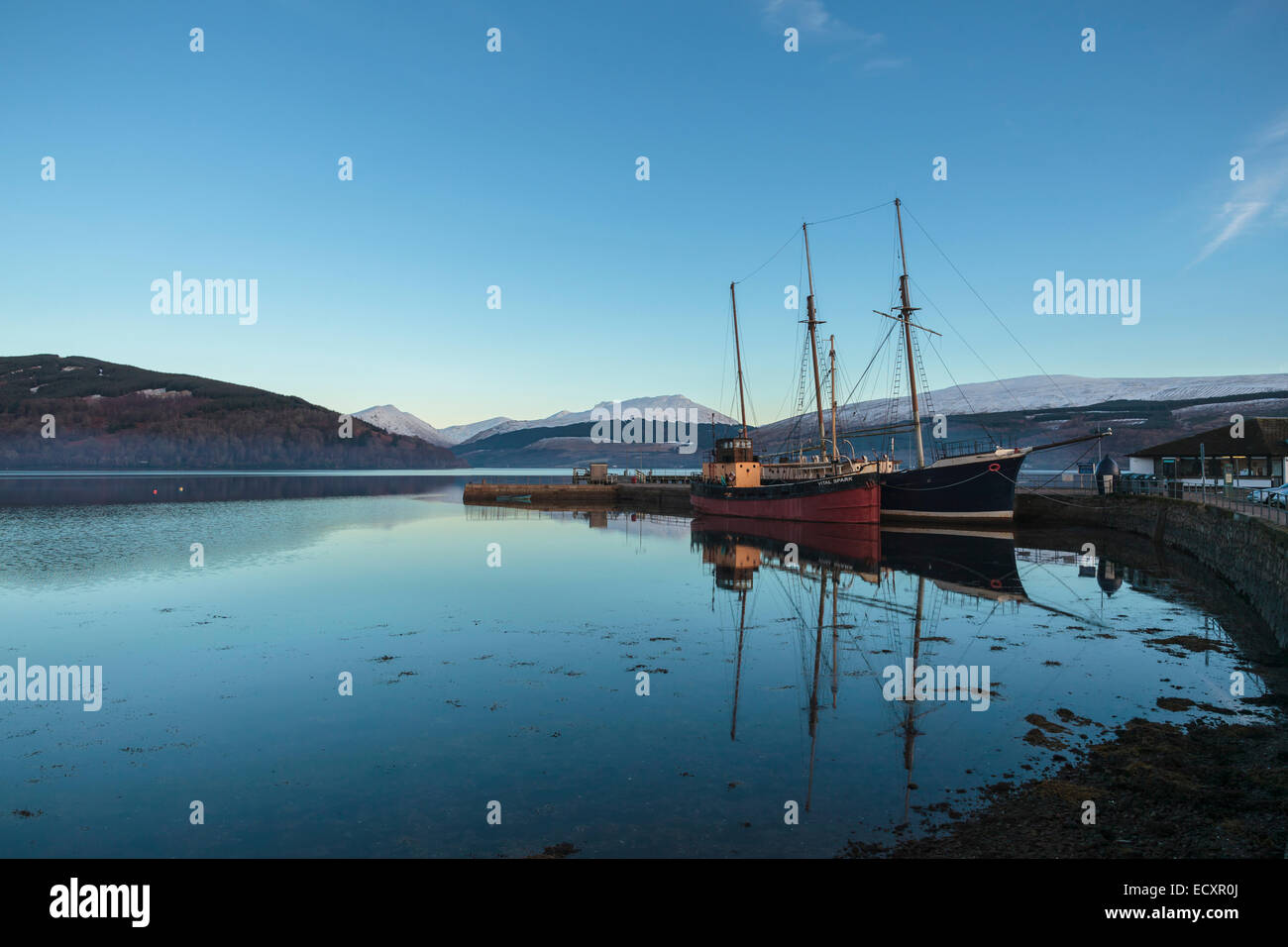 Commercial fishing boats sit in the harbour of Inverary on Loch Fyne.  Snow covers the peaks of the Scottish Highlands, Scotland Stock Photo